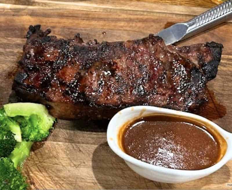 Close-up of a juicy grilled prime steak served with a side of house-made brown sauce and steamed broccoli on a wooden cutting board at Ciao Ragazzi in Chicago.